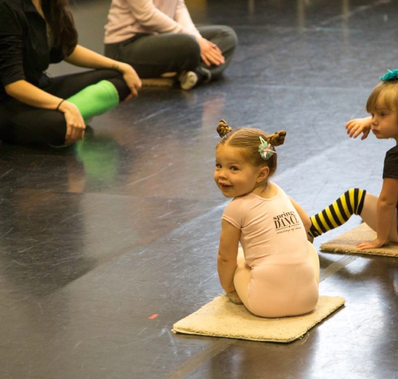 A young pre-school dancer smiling at the camera as she prepares to begin the ballet portion of her class
