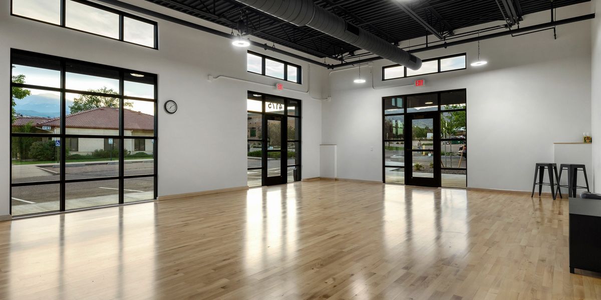 A large studio with wood paneled floors and floor to ceiling windows, providing a great view of Pikes Peak