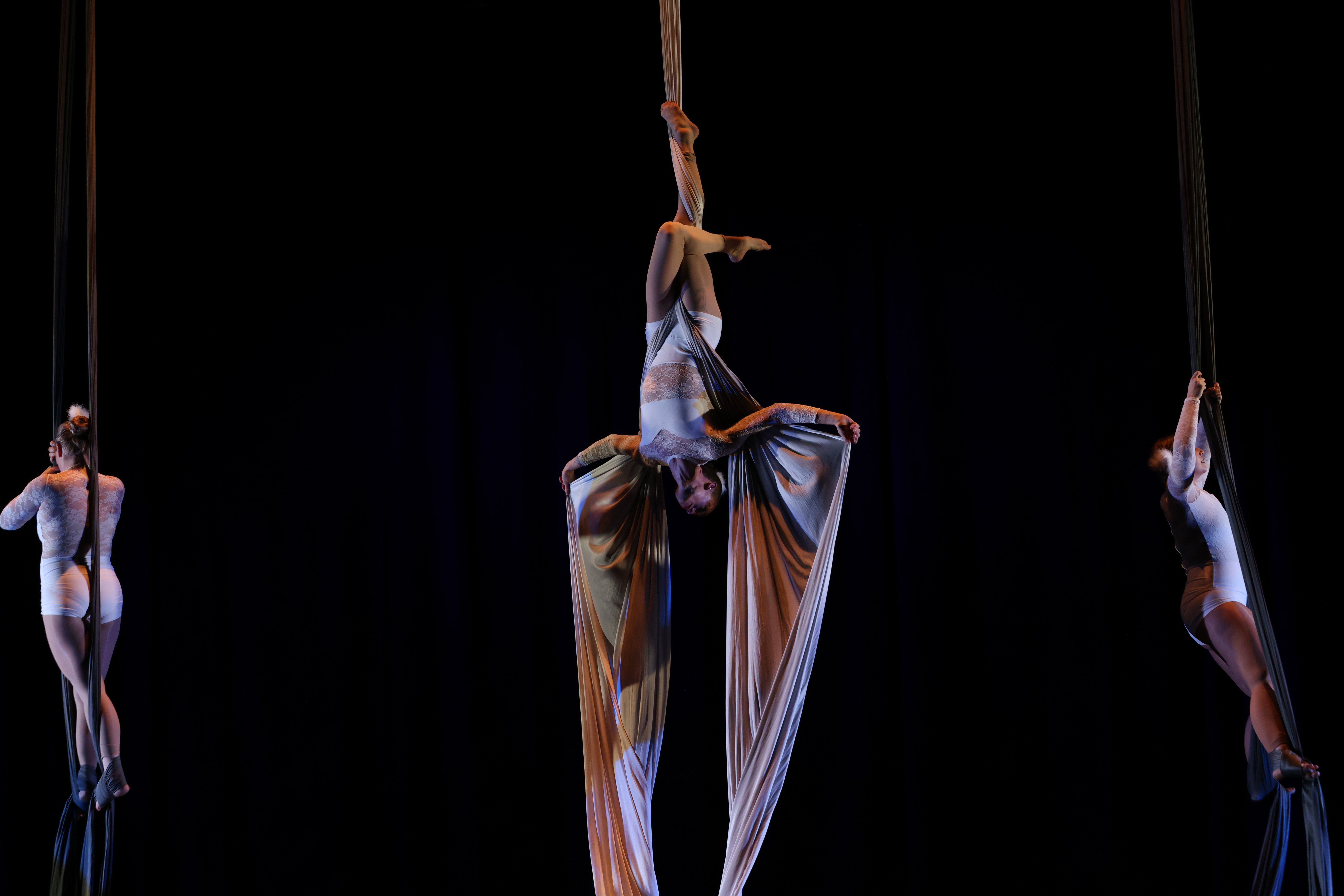 Soloist in white costume hanging upside down in the silk